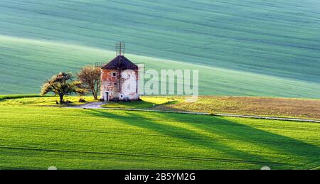 Splendido paesaggio rurale con antico mulino a vento e verdi colline di primavera. Regione Della Moravia Meridionale, Repubblica Ceca Foto Stock