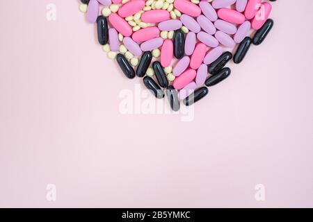 Farmaci colorati sparsi pillole a forma di cuore su uno sfondo rosa. Capsule di pillole antibatteriche per antibiotici. Idea creativa. Medicina. Farmaci. Foto Stock