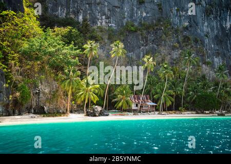 Spiaggia isolata e remota con capanna sotto le palme sull'Isola di Pinagbuyutan. Incredibili rocce di pietra calcarea, spiaggia di sabbia, acque turchesi della laguna blu. Foto Stock