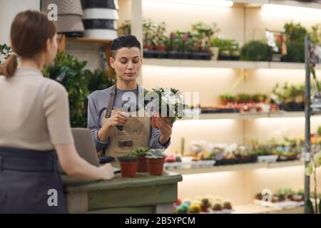 Girovita ritratto di giovane donna moderna che vende fiori al cliente in negozio di fiori e scansione codice a barre, copia spazio Foto Stock