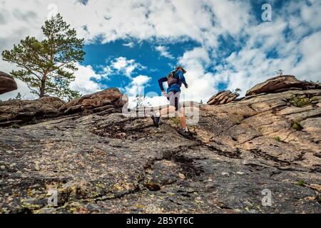 Corridore corre nelle montagne rocciose. Un uomo in un maglione blu e pantaloncini neri sta allenando all'aperto Foto Stock
