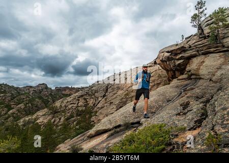 Corridore corre sulle montagne rocciose. Un uomo in Jersey blu e pantaloncini neri sta allenando all'aperto Foto Stock