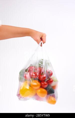 Mano della donna che tiene sacchetti di plastica di verdure su sfondo bianco Foto Stock