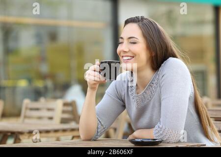 La donna felice soddisfatta che ha odorato la sua tazza di caffè seduto su una terrazza del caffè Foto Stock