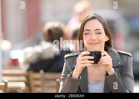 Vista frontale ritratto di una donna soddisfatta che odorava una tazza di caffè su una terrazza del ristorante Foto Stock