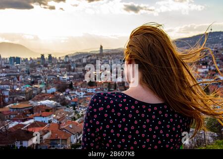 Ragazza che guarda alla città di Sarajevo dal bastione giallo mentre il vento soffia nei capelli Foto Stock