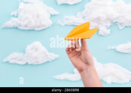 Piano di carta arancione nella mano del bambino che vola attraverso il cielo blu con le nuvole Foto Stock