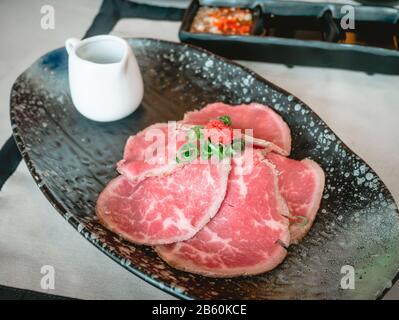 Fette di manzo wagyu con salsa ponzu in un piatto di ceramica nera sul tavolo giapponese nel ristorante. Foto Stock