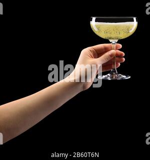 Donna mano che tiene un bicchiere di champagne frizzante isolato su nero. Foto Stock