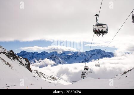 Gli sciatori al Passo del Tonale, nelle Alpi italiane, salano lo skilift sopra la nebbia ondulata nel febbraio 2020. Foto Stock