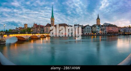 Vista panoramica della famosa chiesa Fraumunster, del ponte Munsterbrucke e del fiume Limmat al tramonto, della città vecchia di Zurigo, la città più grande della Svizzera Foto Stock