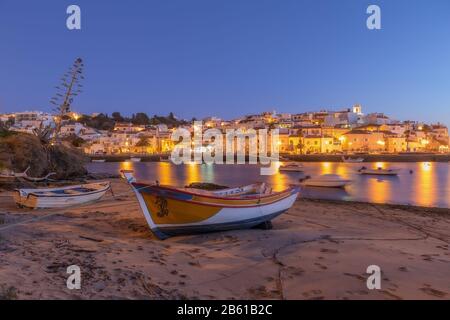 Villaggio di pescatori, Ferragudo giallo lanterne luci. Barca tradizionale in primo piano. Foto Stock