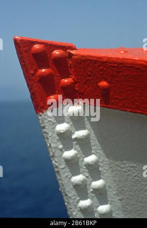 Prua di una barca a Paxos, Grecia, dipinta di rosso e bianco su uno sfondo blu di mare e cielo. I rivetti sulla chiglia gettano ombre sulla vernice. Foto Stock