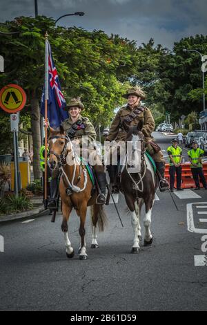 Sandgate Queensland Australia - Aprile 2019. Le donne in uniforme militare portano la bandiera australiana a cavallo per la marcia ANZAC. Foto Stock