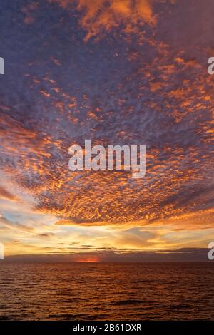 Il sole che tramonta illumina drammaticamente le basse nuvole in una serata di Summers sulle acque calme del Mare d'Irlanda del Sud. Foto Stock