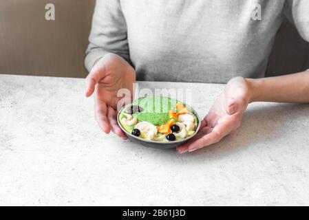 Mangiate una ciotola sana per la colazione. Frullato verde, granola, noci e frutta in ceramica ciotola in mani femminili. Cibo pulito, dieta, detox, vegetariano, verdure Foto Stock