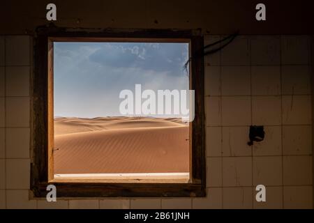 guardando fuori dalla finestra di una casa abbandonata nel deserto e all'orizzonte una tempesta di pioggia che si avvicina con raggio di luce Foto Stock