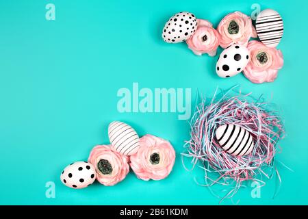 Nido decorativo con uova grafiche creative e fiori ranunculus su sfondo pastello blu. Concetto di Pasqua. Inserire il testo. Foto Stock