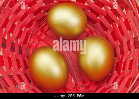 Tre uova d'oro di Pasqua in un cestino rosso, primo piano. Foto Stock