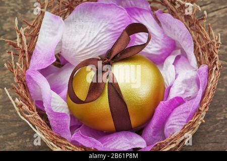 Uovo d'oro di Pasqua con nastro marrone in un nido su una tessitura di legno. Foto Stock
