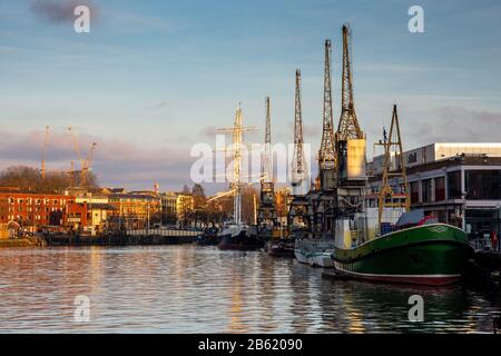 Bristol, Inghilterra, Regno Unito - 29 dicembre 2019: Il sole serale splende su barche, gru e magazzini convertiti sui vecchi Bristol Docks. Foto Stock