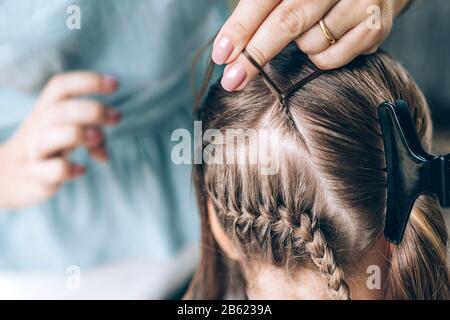 La madre fa la treccia dei capelli alla sua figlia, la foto di primo piano. Foto Stock