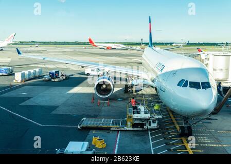 New York City, USA - 4 agosto 2018: Carico e scarico di merci da parte dei lavoratori in aereo Delta Air Lines parcheggiato all'aeroporto internazionale John F. Kennedy (J. Foto Stock