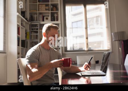 Vista laterale uomo con caffè utilizzando smartphone e computer portatile Foto Stock