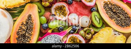 Freschi frutti esotici e tropicali di foglie di palma sul pastello sfondo arancione - papaie, manghi, ananas, frutto della passione, dragon frutta, uva, lichee, kiwi Foto Stock