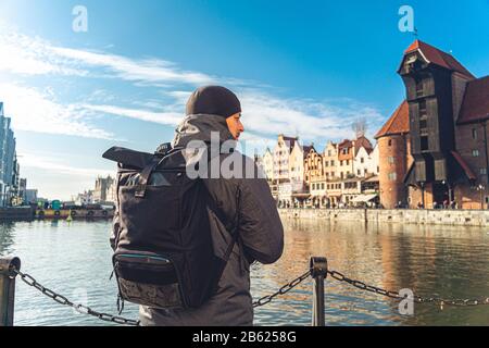 Tema del turismo in Polonia. Viaggiare a Danzica. Un viaggiatore maschio usa un telefono sull'argine del fiume Mottawa in mezzo all'attrazione principale, un Foto Stock