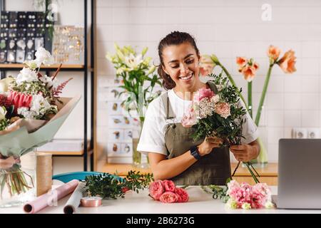 Fiorista felice femminile che prepara un bouquet nel suo negozio. Donna sorridente che tiene i fiori al banco. Foto Stock
