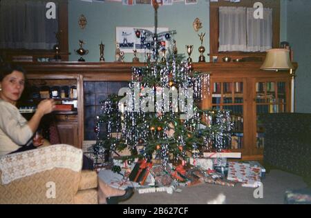 Donna seduta accanto ad un piccolo albero di Natale in un soggiorno ca. 1957-1960 Foto Stock