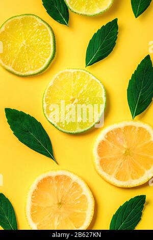 Scorze di limone e lime e motivi di erbe di menta su fondo giallo. Vista dall'alto. Sfondo di design minimo. Foto Stock