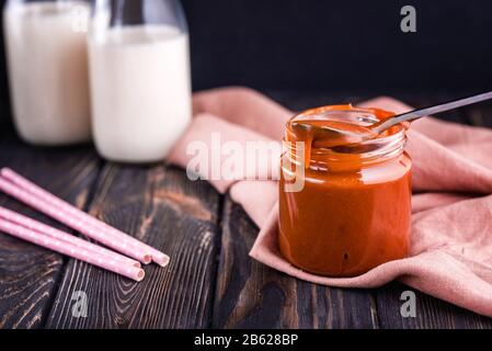 Caramello salato fatto in casa su una tavola scura con un bel cucchiaio nero e latte. Delizioso dessert per colazione. Foto Stock