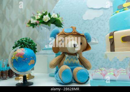 Orsacchiotto con cappello e occhiali da aviatore e un bellissimo bouquet e palloncini blu e bianchi sullo sfondo. Orso con gli occhiali e l'aeroplano d'annata Foto Stock