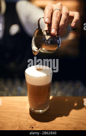 Il barista professionale versa il latte nel caffè preparando il processo di preparazione del caffè. Primo piano foto ritagliate, arte, lavoro, professione Foto Stock