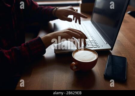 giovane uomo che lavora duro usando il laptop mentre ha pausa caffè, primo piano vista laterale foto, pastime, hobby, interets. Foto Stock
