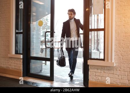 giovane uomo d'affari attraente nei vestiti di moda che entrano, andando alla costruzione dell'ufficio, giorno lavorativo, l'uomo che è in ritardo, l'uomo va dentro, all'interno, pieno Foto Stock