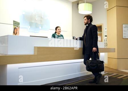 giovane e attraente uomo barbuto che fa il tifo per l'hotel. foto vista laterale. sconti, vendita, ragazzo che sceglie una camera Foto Stock