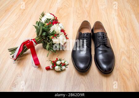 Mattina dello sposo. Accessori per matrimoni in colori rossi. Scarpe, bouquet di nozze, boutonniere su sfondo di legno. Foto Stock