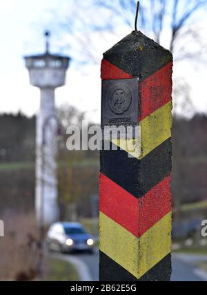 09 marzo 2020, Turingia, Mödlareuth: Un posto di confine con lo stemma della Repubblica democratica tedesca e una torre di guardia nel centro del paese. Il villaggio di 50 abitanti al confine tra Baviera e Turingia era, come Berlino, diviso in due da un muro per decenni. A 100 metri, l'edificio alto più di tre metri è rimasto nel villaggio come parte del museo tedesco-tedesco. Foto: Martin Schutt/dpa-Zentralbild/dpa Foto Stock