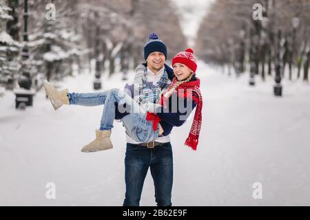 Il ragazzo sollevò la ragazza sulle mani. Concetto di amore invernale. Foto Stock