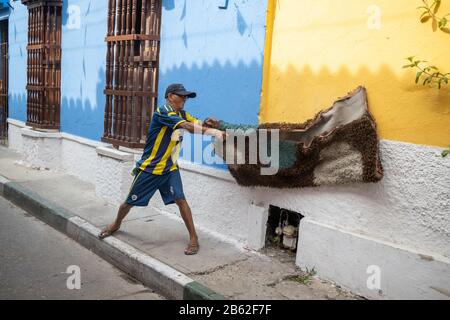 La vita continua in questa trafficata area turistica di Getsemani, l'uomo pulendo la polvere da un tappeto. Foto Stock
