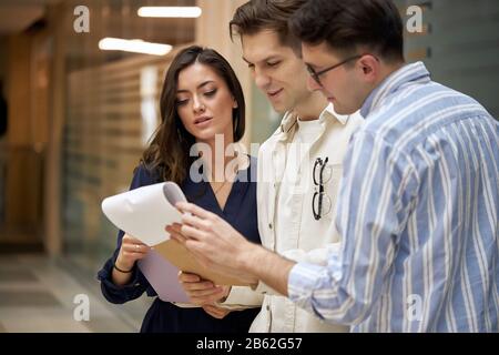 impressionante gente attiva di affari che discute il contratto, il documento, la donna del brunette in camicia elegante blu sty lish e i suoi due bei colleghe che tengono un Foto Stock
