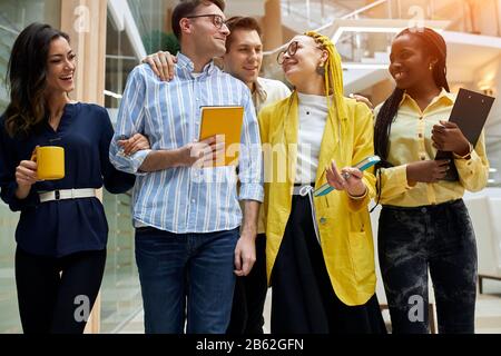 divertenti giovani che si divertono in ufficio, dicendo scherzi mentre camminano, giovane poeple che va a pranzo. Foto Stock