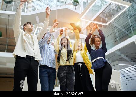Gruppo di sorridenti multirazzial business persone con le braccia in su. Vista bassa, felicità, entertainmnet, lavoratori di ufficio che hanno divertimento, gioia Foto Stock