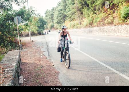 Giovane donna carina con zaino e casco viaggia con la bicicletta all'aperto sulla strada asfaltata Foto Stock