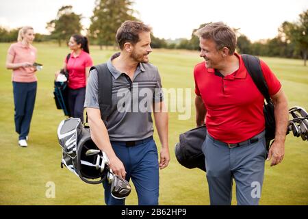 Due Coppie Mature Giocando Rotonda Di Golf Che Trasporta I Sacchetti Di Golf Lungo Il Fairway Foto Stock