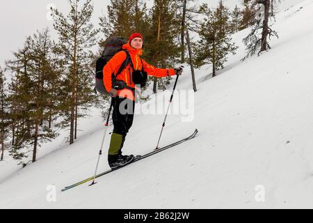Sciatore Mountain hiker sale su una collina molto ripida, con uno zaino pesante. Unguento e sci di Camus permettono di non scivolare giù Foto Stock