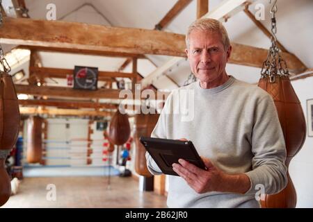Ritratto Di Senior Male Boxing Coach In Gym Tracking Training Con Digital Tablet Foto Stock